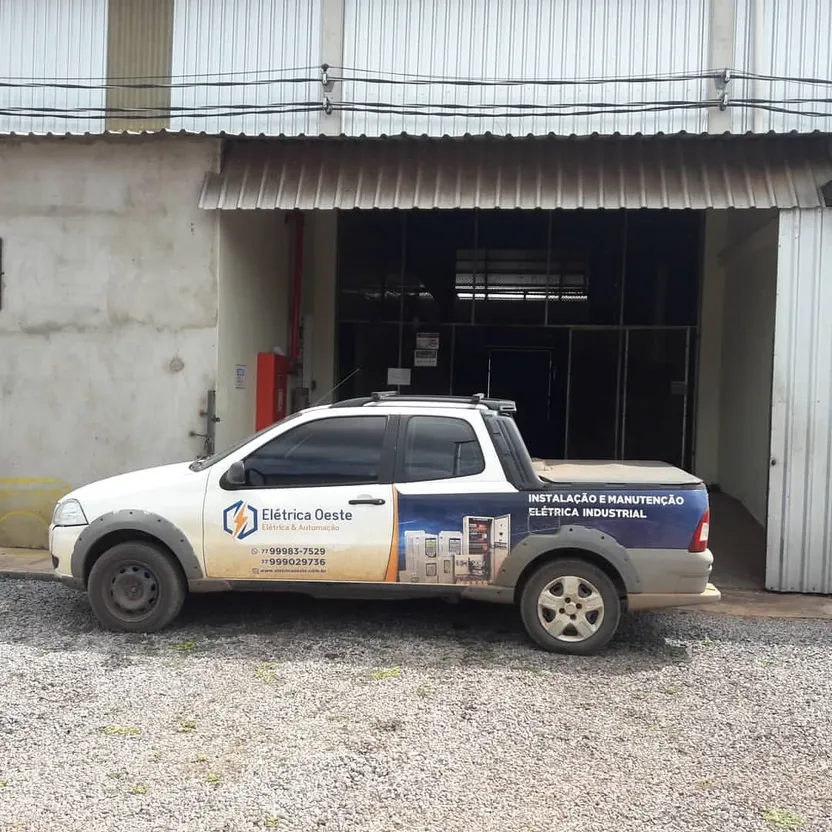 Caminhonete identificada da Elétrica Oeste estacionada diante da entrada de um galpão industrial.