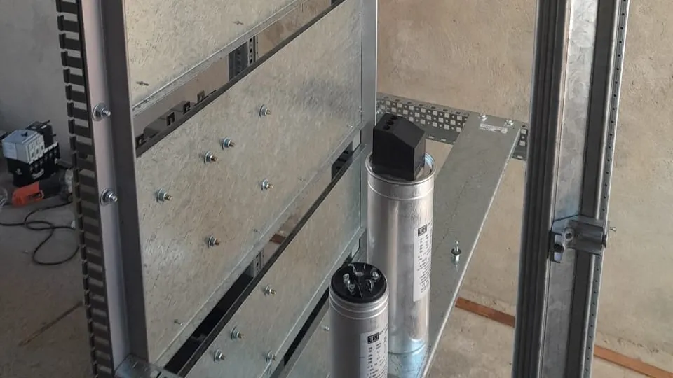 Duas células capacitivas apoiadas na estrutura metálica de um painel em montagem, durante a fabricação de um banco de capacitores.