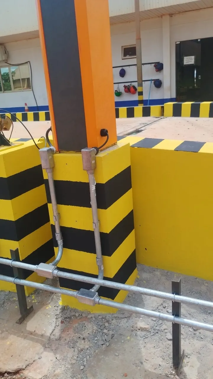 Eletrodutos galvanizados com caixas de passagem fixados em um pilar industrial sinalizado com faixas amarelas e pretas de proteção.