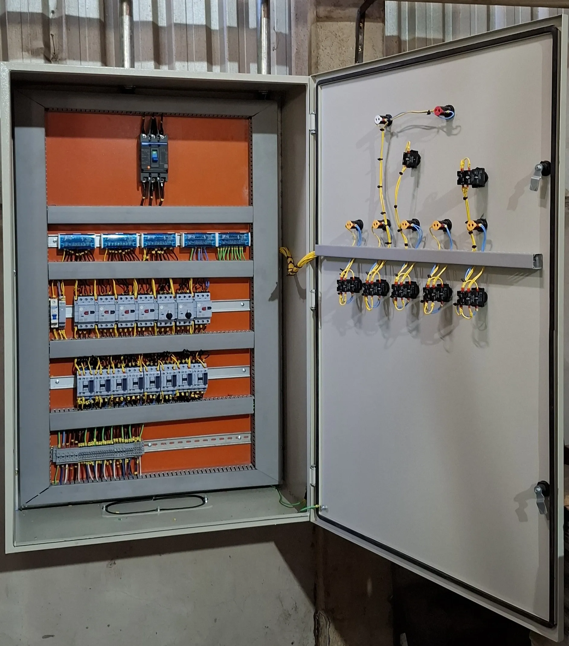 Painel industrial de parede aberto, com disjuntor, módulos de relé, disjuntores-motor e contatores cabeados; na porta, botoeiras e sinaleiros de comando.