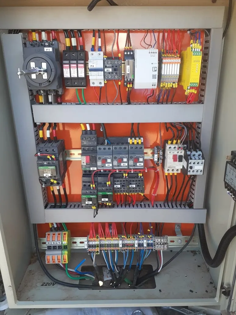 Quadro de comando industrial aberto, com seccionadora, DPS, contatores e relé de segurança sobre a placa de montagem.