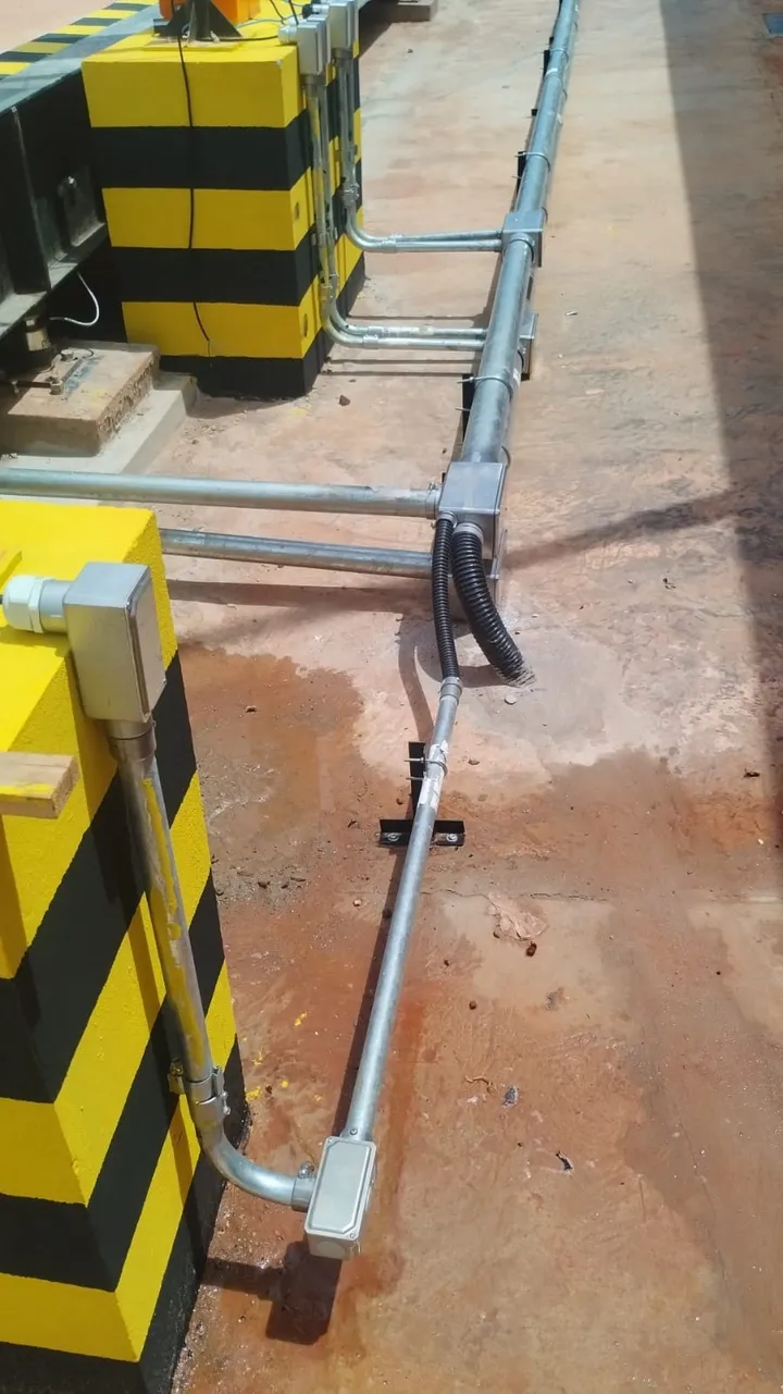 Rede de eletrodutos galvanizados com curvas, conexões e suportes fixados sobre piso industrial.
