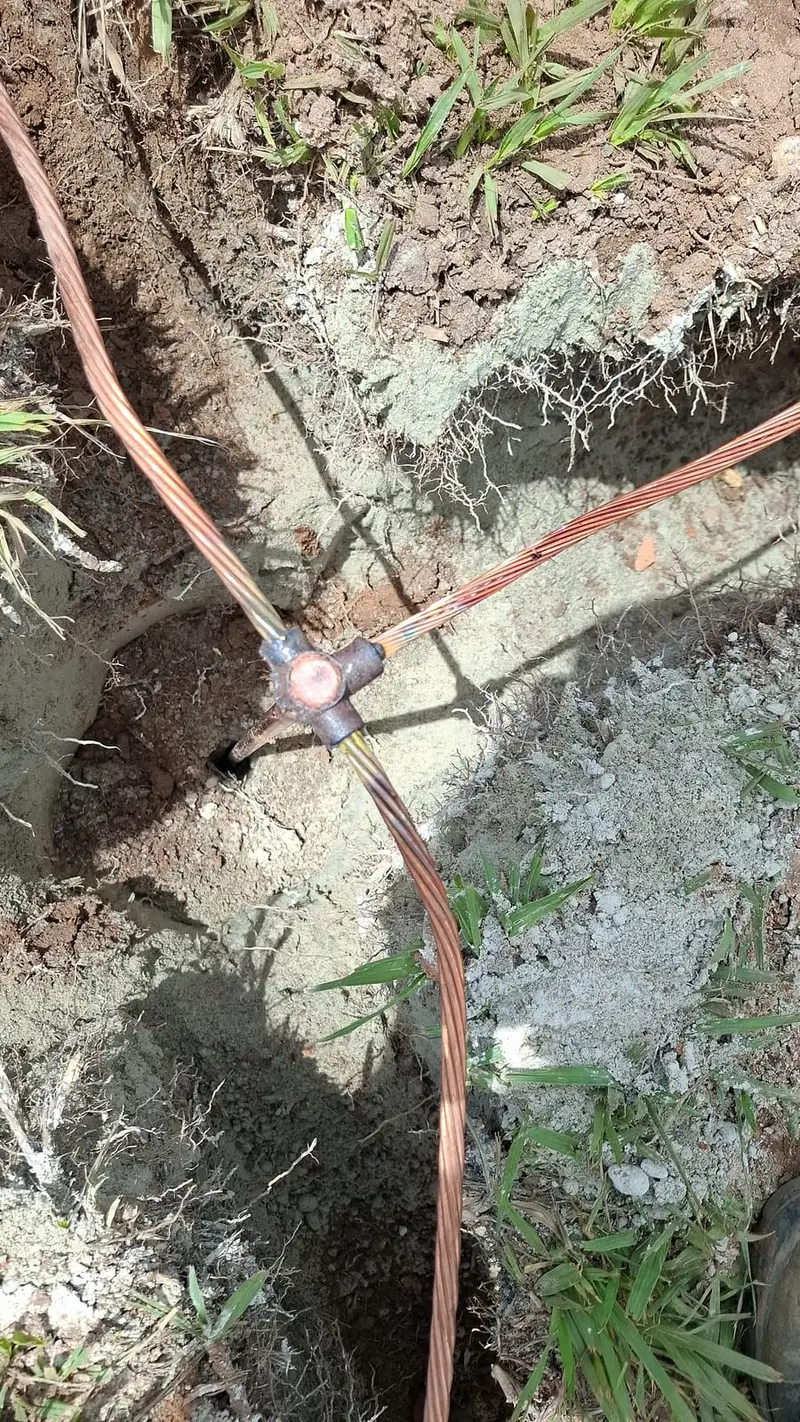 Conexão de solda exotérmica entre cabos de cobre nu, em vala de aterramento aberta no solo.